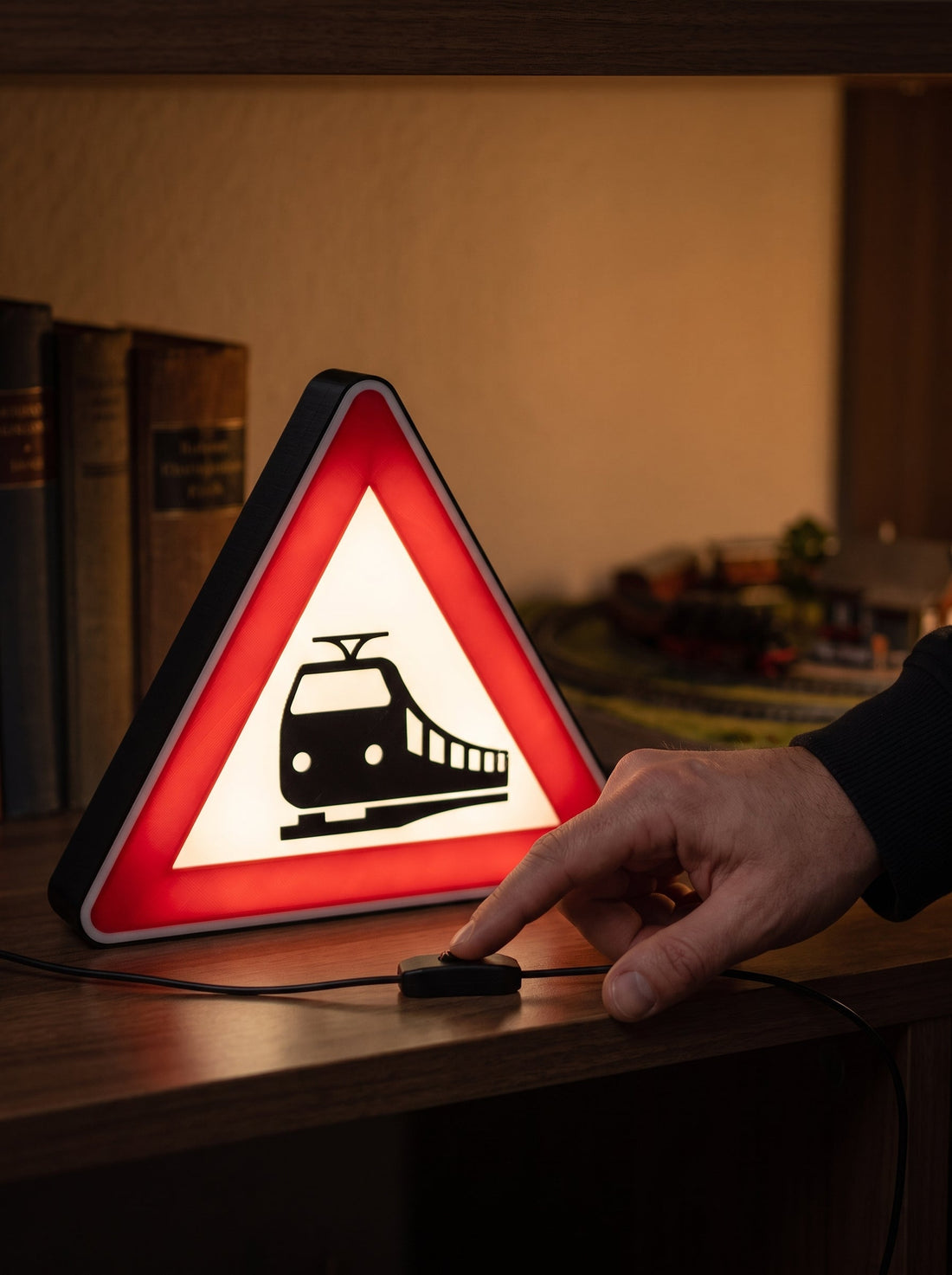 Hand am Schalter im Kabel einer leuchtenden Bahnübergang-Lampe auf einem Regalbrett